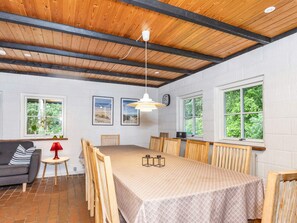 A dining area with a long table, chairs, a hanging light fixture, and a view of greenery through the windows. - 6 Person Holiday Home in Bindslev (Bindslev)
