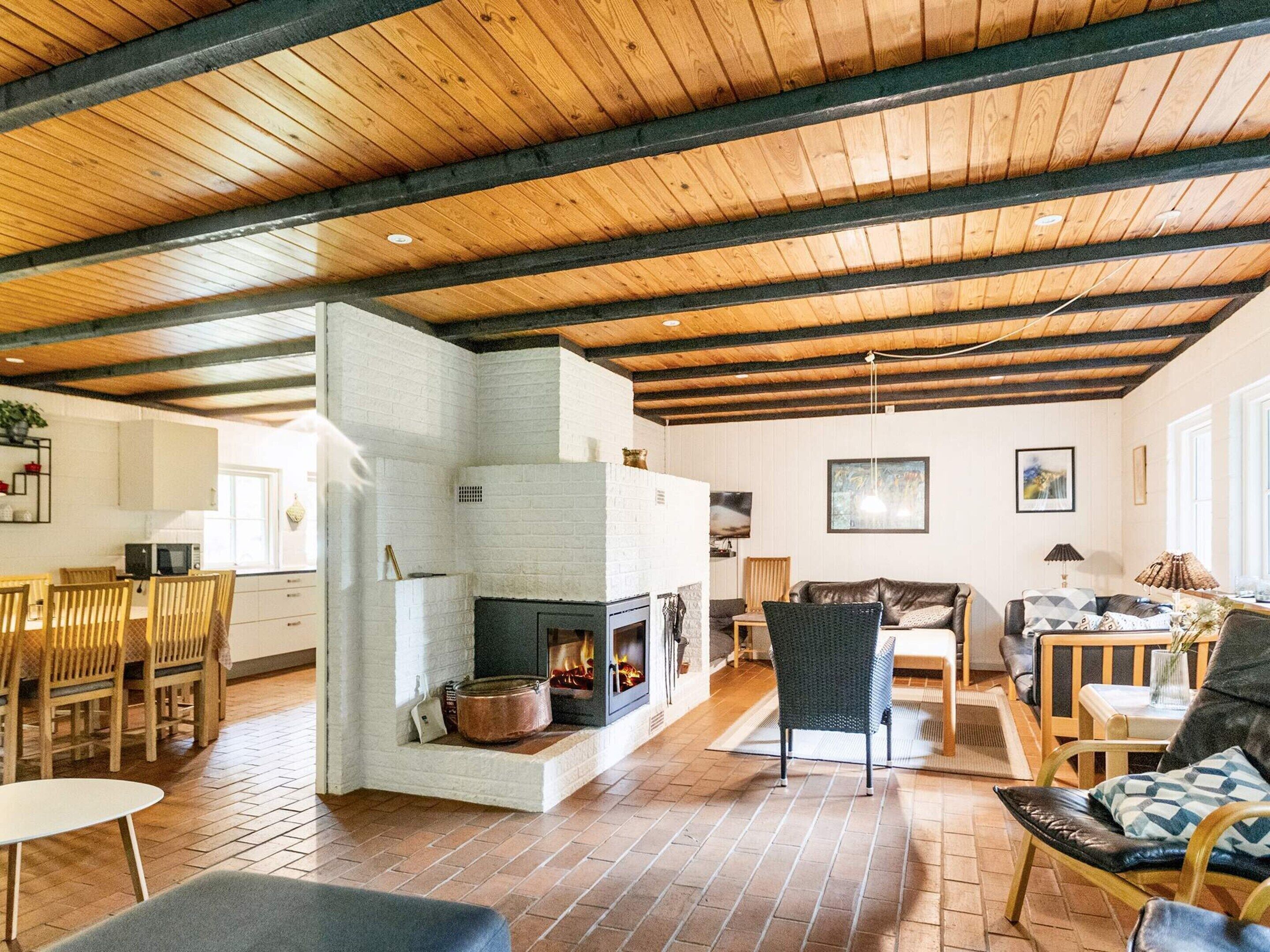 Un vaste espace de vie doté d’une cheminée, de poutres apparentes en bois au plafond et d’un coin repas avec des chaises et une table.