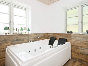 A modern bathroom with a large white bathtub, wooden paneling, and decorative trees on the windowsill. - 10 Person Holiday Home in Glesborg (Glesborg)