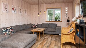 A cozy living room with a grey sectional sofa, a wooden coffee table, a wicker chair, and a window with a view of greenery. - 10 Person Holiday Home in Glesborg (Glesborg)