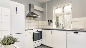 A modern kitchen with white cabinetry, a built-in oven, a stainless steel range hood, and a window providing natural light. - Holiday Home in Holeby (Holeby)