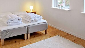 A bedroom with two beds, a bedside table with a lamp, a window with a view, and a white rug. - Holiday Home in Holeby (Holeby)