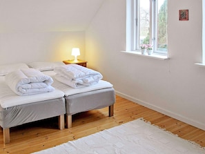A bedroom with two beds, a bedside table with a lamp, a window with a view, and a white rug. - Holiday Home in Holeby (Holeby)