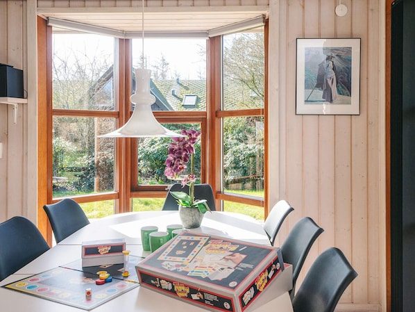 A room with a large bay window, a table with a board game, chairs, a hanging light fixture, and a framed picture on the wall.
