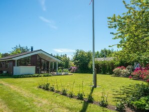 A house with a covered porch, a flagpole, and a well-maintained garden with various plants and flowers. - 4 Star Holiday Home in Ulfborg (Ulfborg)