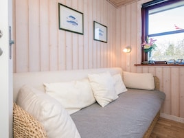 Et værelse med en væg af træpaneler, en sofa med puder, et indrammet billede, et vindue med udsigt og en vægmonteret lampe.
