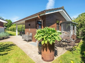 A wooden cabin with a covered patio, outdoor seating, and a large potted plant.
