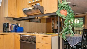 A kitchen with wooden cabinets, a stove, and a dining area with a table and chairs. - 6 Person Holiday Home in Romo (Rømø)