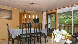 A dining area with a wooden table and chairs, a cabinet with glass doors, and a view of the outdoors through a large window. - 6 Person Holiday Home in Romo (Rømø)
