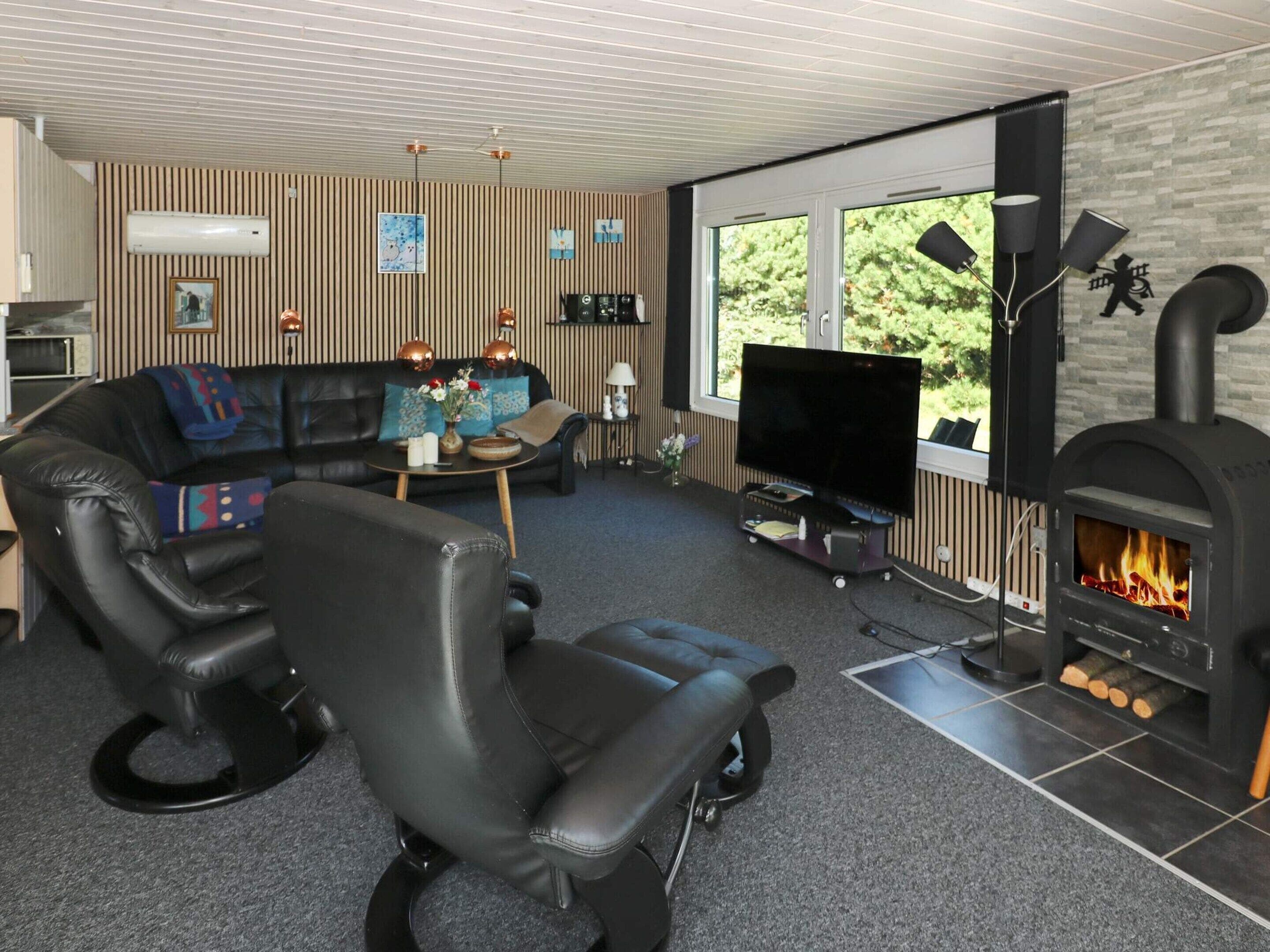 Una sala de estar moderna con un sofá de cuero, un sillón negro, un televisor de pantalla plana, una chimenea y un ventanal grande.