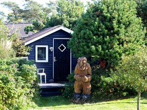 A wooden sculpture of a bear in front of a small blue house with a white door and a window.