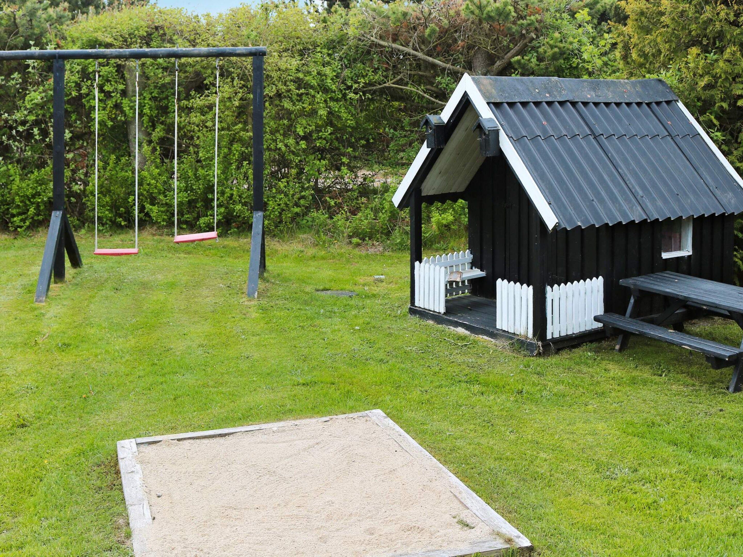 Een speeltuin met schommels en een klein houten bouwwerk met een bankje.