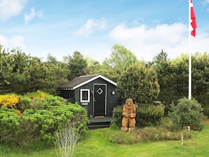 A small cabin with a black door and window, surrounded by greenery and a flagpole. - 6 Person Holiday Home in Hadsund (Hadsund)