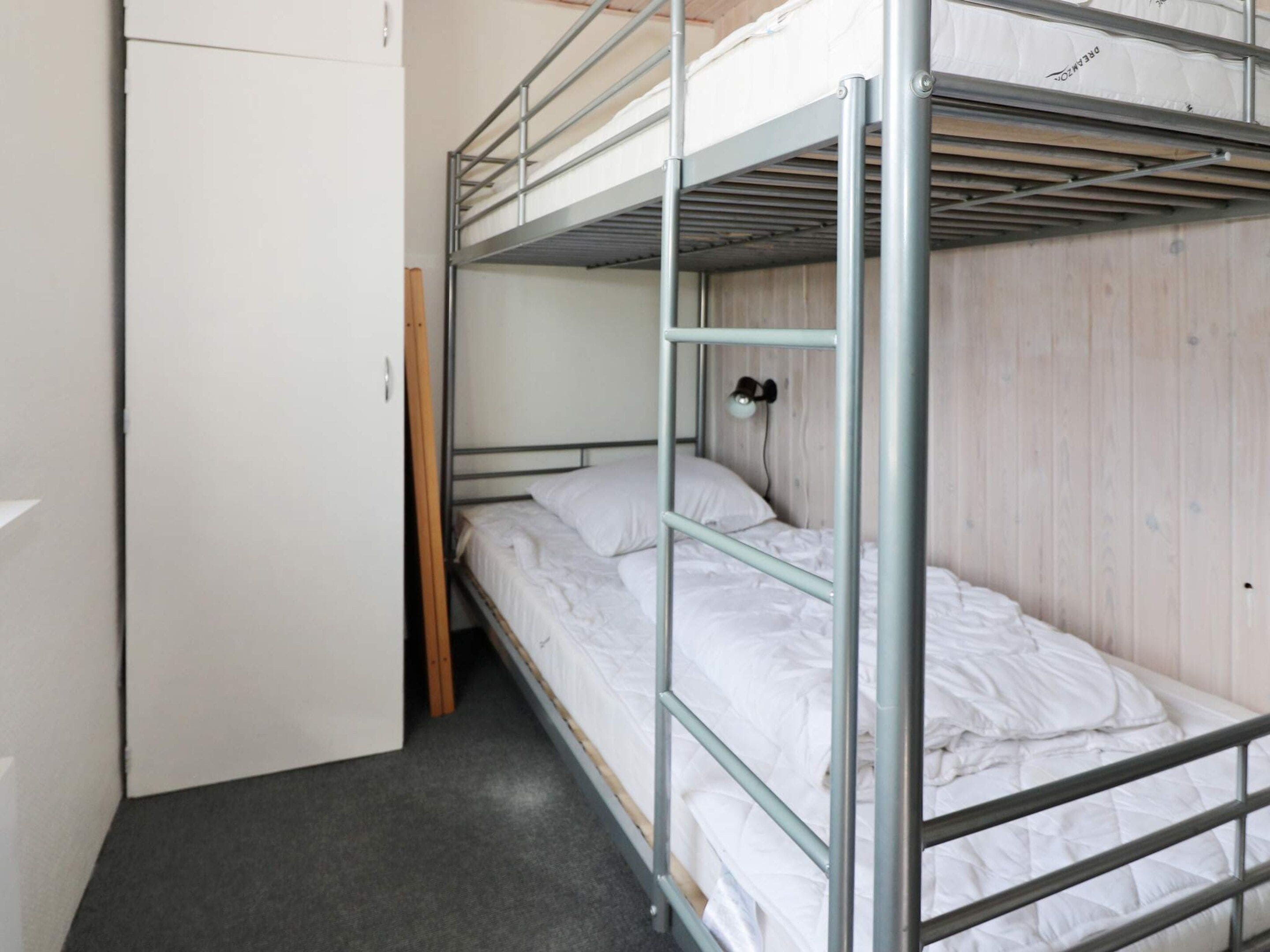A bunk bed room with a wooden wardrobe and a wall-mounted lamp.