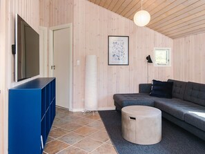 A modern living room with a large flat-screen TV, a grey sectional sofa, a round ottoman, and a framed artwork on the wall. - 5 Star Holiday Home in Sjolund (Sjølund)