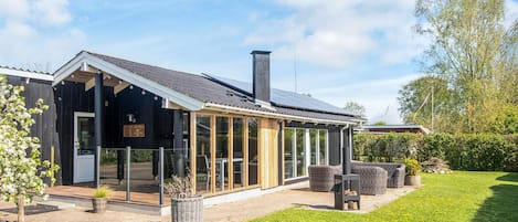 A modern house with a large glass extension, a chimney, and a well-maintained lawn.