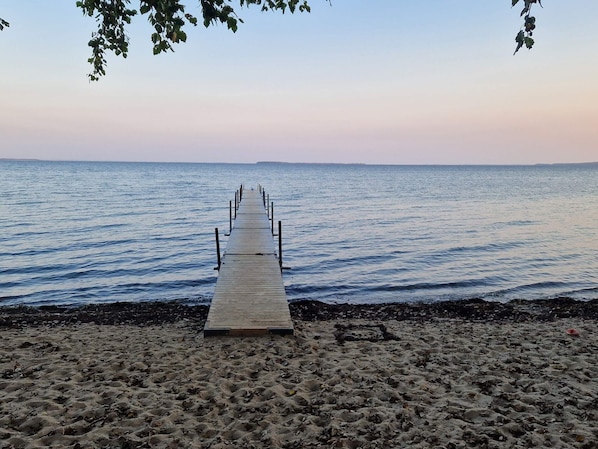 A wooden pier extending into calm water, surrounded by sandy beach.