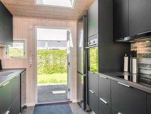 A modern kitchen with a built-in oven, a stainless steel sink, and a window overlooking a garden. - 5 Star Holiday Home in Sjolund (Sjølund)