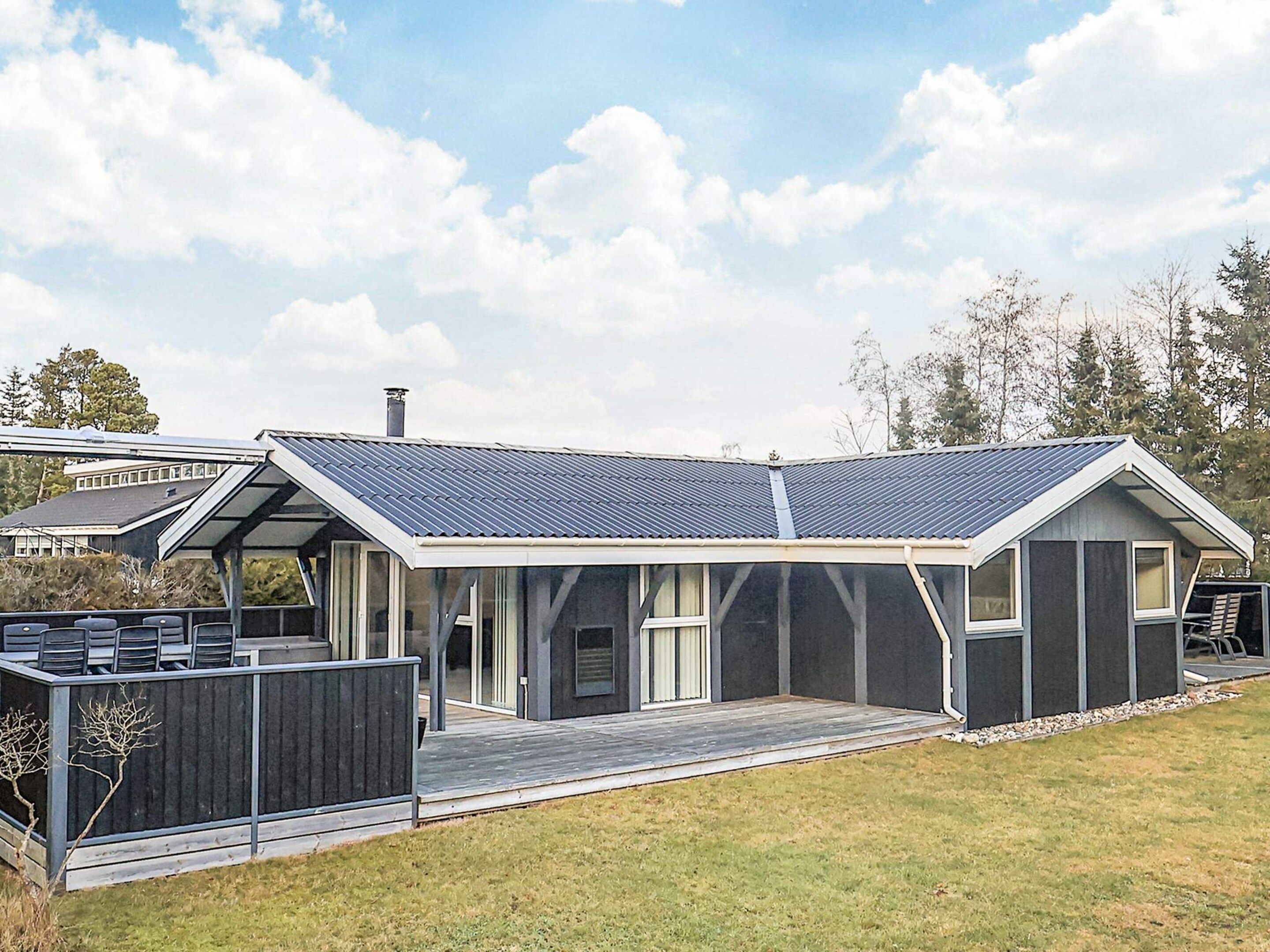 Ein modernes Haus mit überdachter Terrasse, großen Fenstern und einem geneigten Dach.