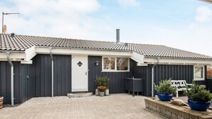 A residential building with a tiled roof, a dark facade, a white door, and a paved courtyard with potted plants. - 4 Star Holiday Home in Ebeltoft (Ebeltoft)