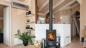 A cozy living room with a central fireplace, wooden beams, and a white radiator. - 4 Star Holiday Home in Ebeltoft (Ebeltoft)