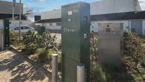 Caixa de serviços identificada com a etiqueta 'Clever', uma lâmpada de rua próxima, tudo em frente a um edifício sob um céu limpo.