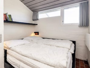 A single bed with a headboard, a bedside lamp, a window with curtains, and a shelf with books. - 6 Person Holiday Home in Brovst (Brovst)