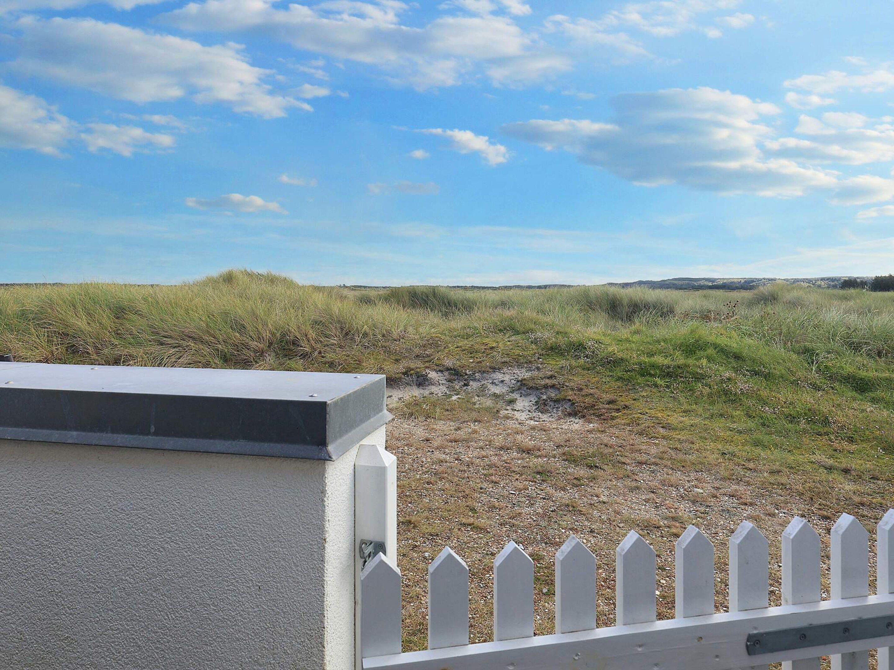 Et hvidt stakhegn, en betonkonstruktion og en græsmark under en klar himmel.