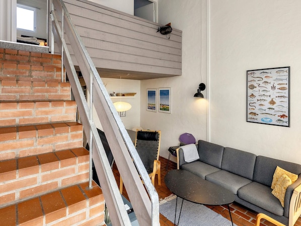 A staircase leading to an upper level, a grey sofa, a framed fish poster, and a small table. - 6 Person Holiday Home in Brovst (Brovst)