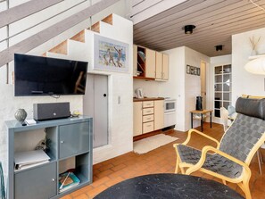 A modern living room with a flat-screen TV, a bookshelf, a dining area with a table and chairs, and a kitchen with cabinets and appliances. - 6 Person Holiday Home in Brovst (Brovst)