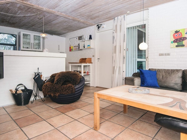 A living room with a sofa, a coffee table, a black furry chair, a tiled floor, a white brick wall, and a window.