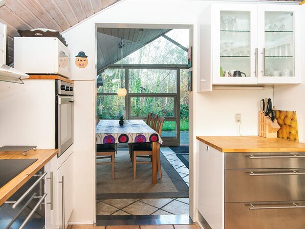 A kitchen with a dining area, a refrigerator, an oven, and a window with a view of greenery.