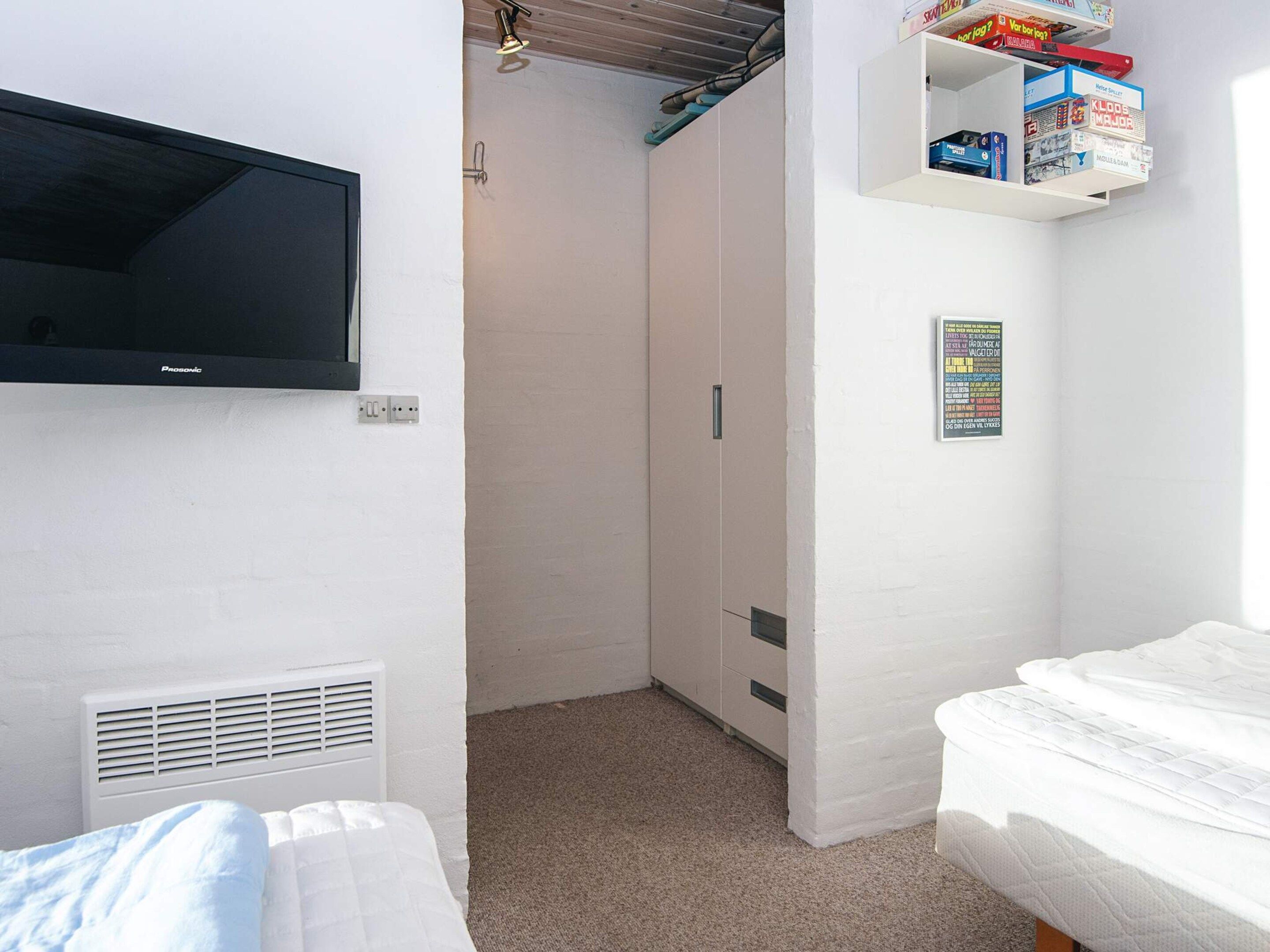 A bedroom with a bed, a TV mounted on the wall, a wardrobe, and a shelf with books.