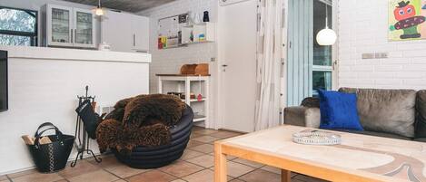A cozy living room with a sofa, a coffee table, and a black furry chair. There's a kitchen area with cabinets and a window.