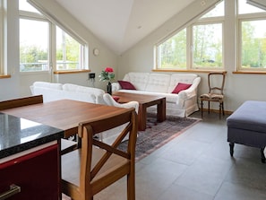 A room with a dining table, white sofas, a wooden chair, and a grey ottoman. - Holiday Home in Onsala (Gottskar)