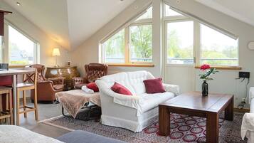 A high-ceilinged room with a white sofa, a wooden table, and a patterned rug.