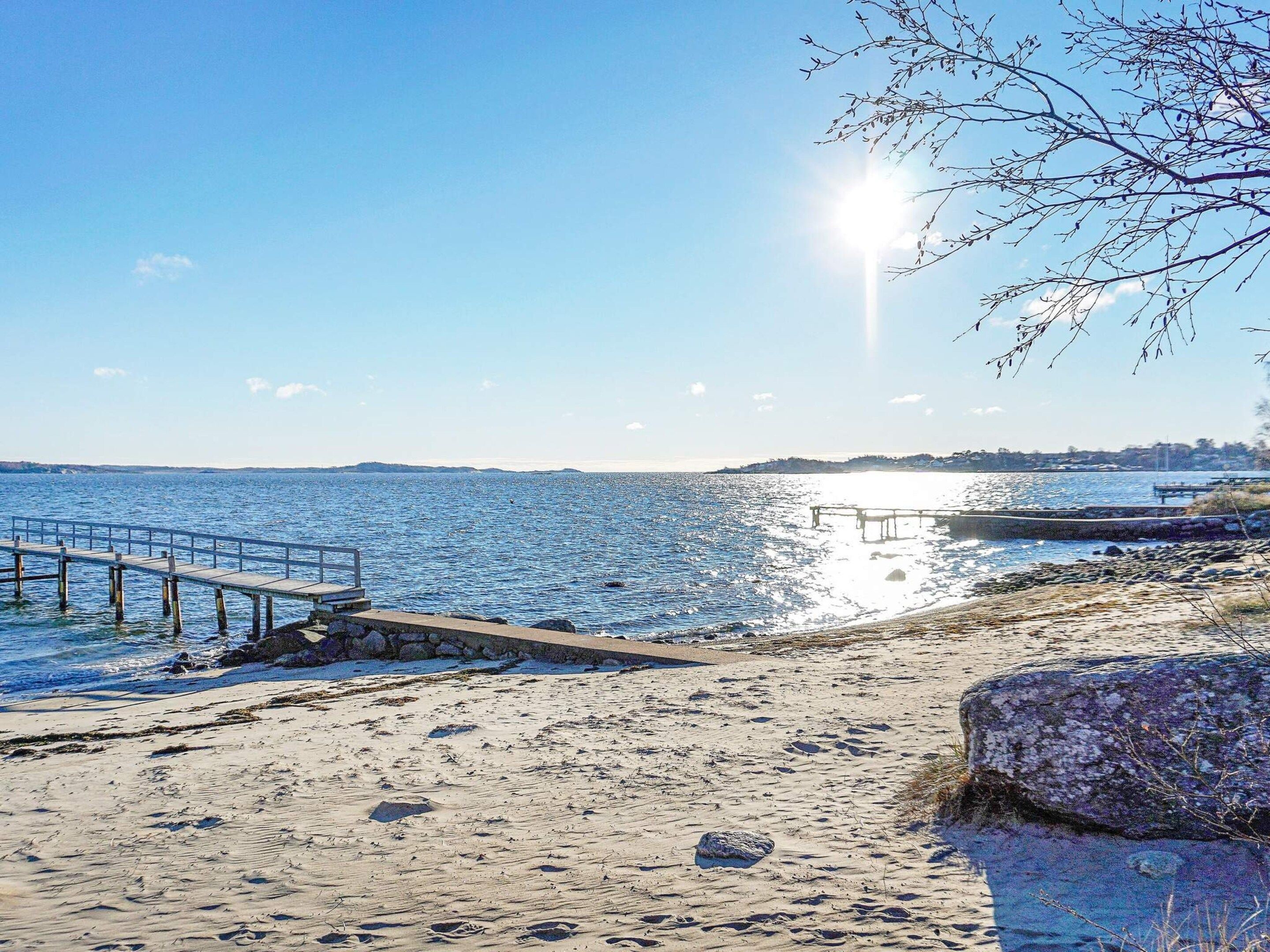 A beach with a wooden pier extending into calm waters, a rocky shoreline, and a clear sky.
