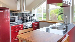 A modern kitchen with red cabinetry, stainless steel appliances, a wooden dining table, and a large window providing a view of greenery outside. - Holiday Home in Onsala (Gottskar)