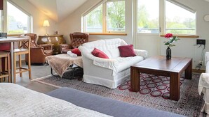 A cozy loft bedroom with a white sofa, a wooden coffee table, and a large window offering a view of greenery. - Holiday Home in Onsala (Gottskar)
