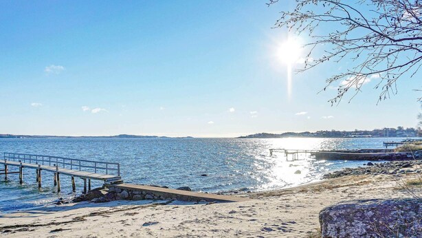 A beach with a pier extending into calm waters, a rocky shoreline, and a clear sky. - Holiday Home in Onsala (Gottskar)