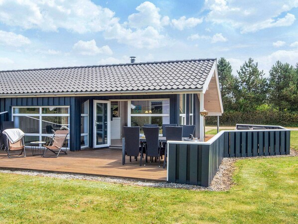 A modern house with a large deck, outdoor seating, and a covered patio area.