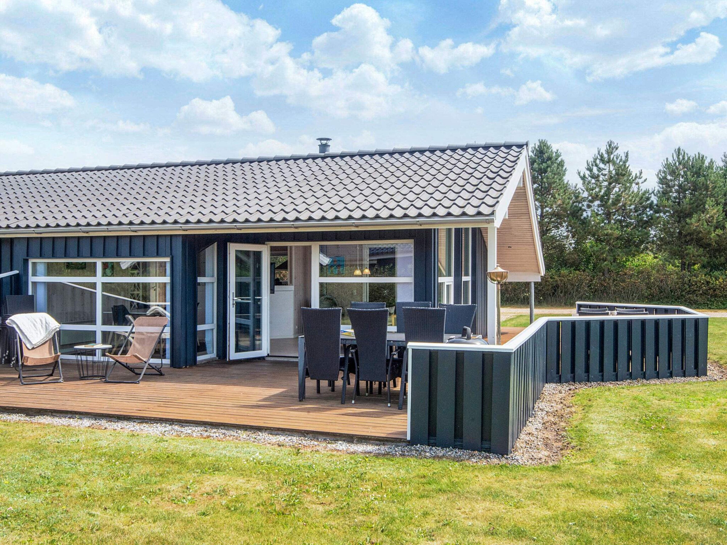 A modern house with a large deck, outdoor seating, and a covered patio area.