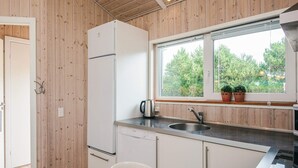 Une cuisine avec des murs en bois, un réfrigérateur blanc, un lave-vaisselle Bosch, un évier avec un robinet et une fenêtre ornée de plantes en pot.