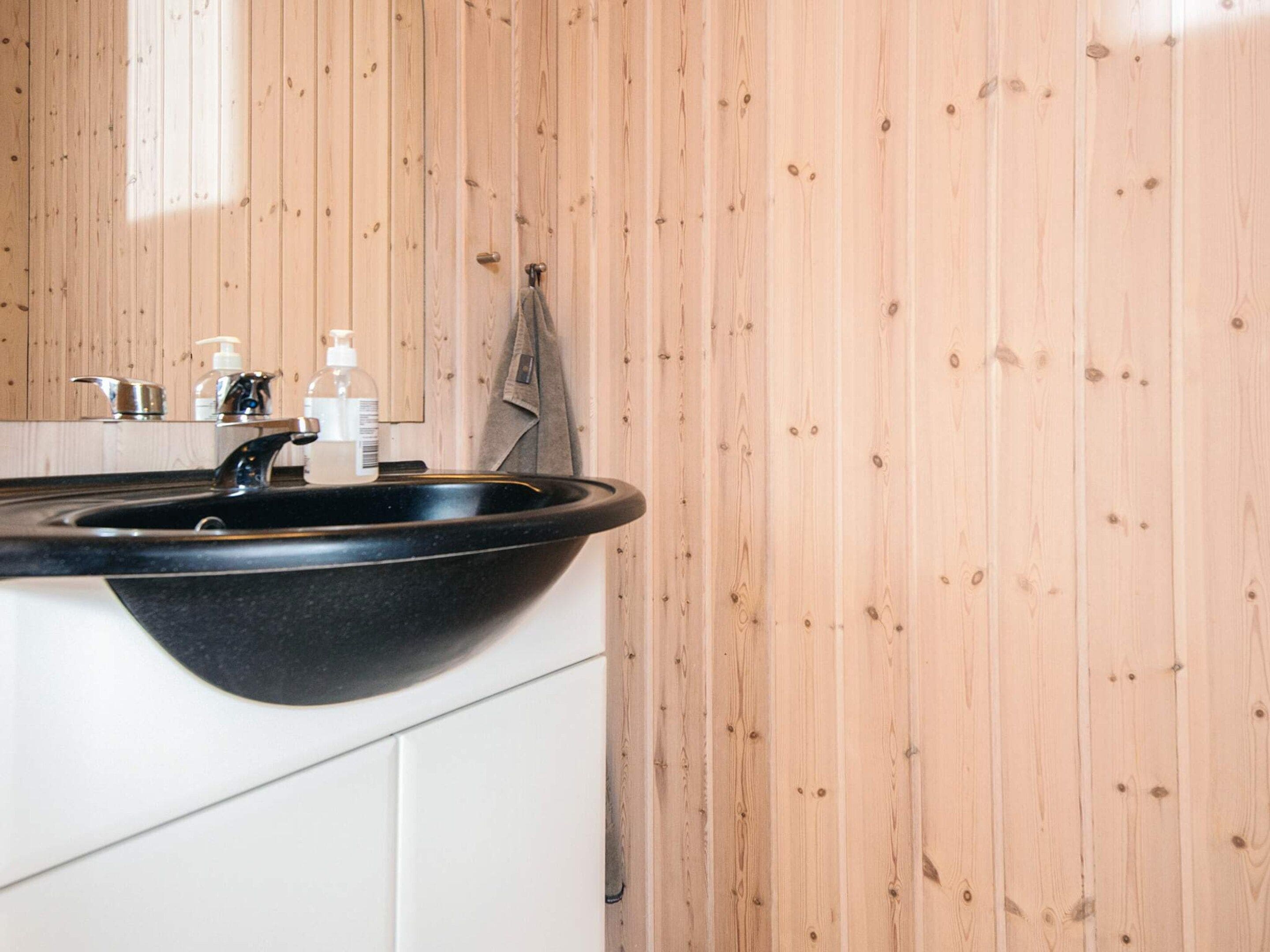 A bathroom with a black basin sink, wooden panel walls, and a towel hanging on the wall.