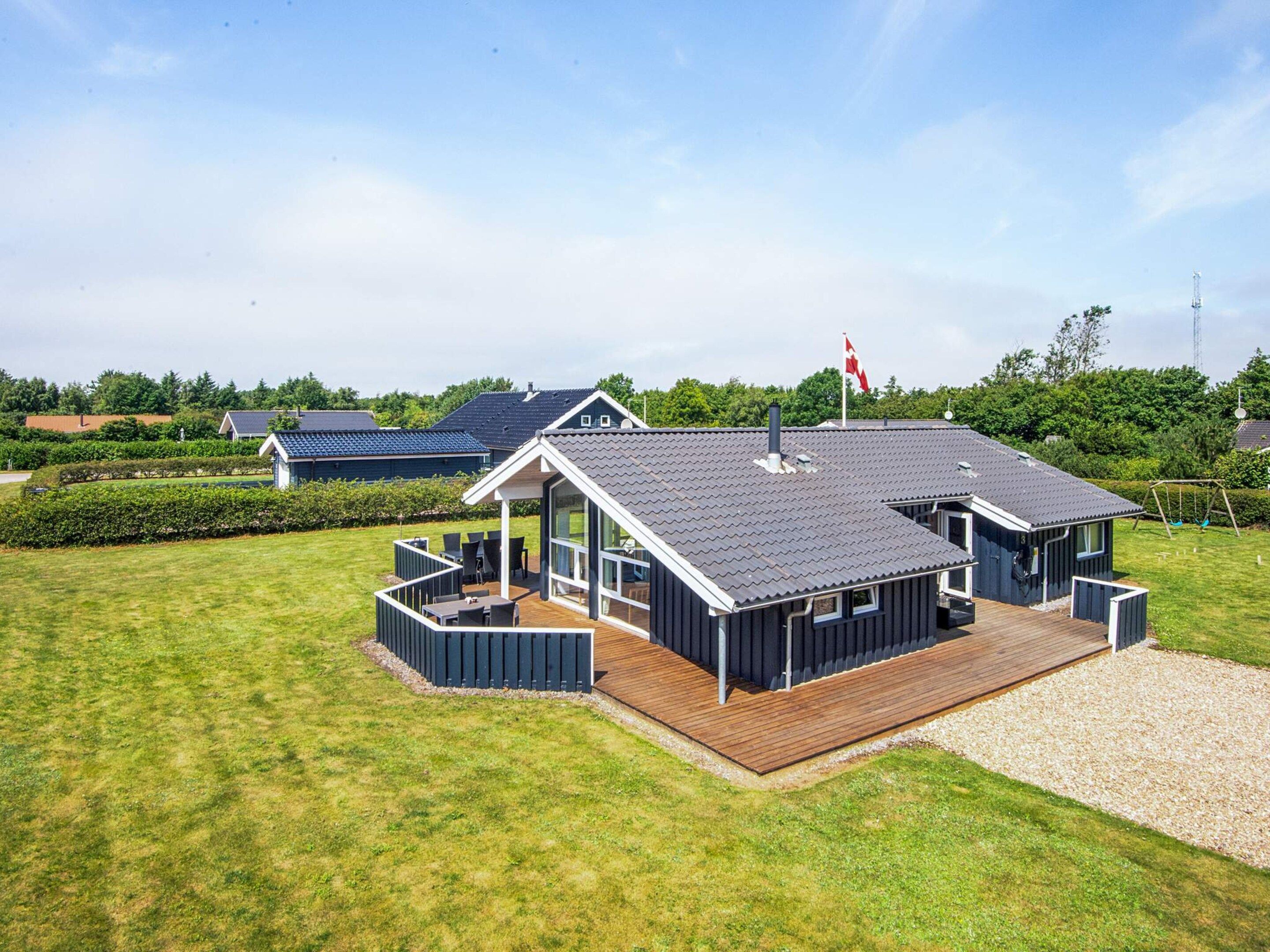 A modern house with a large deck, a covered outdoor area, and a flag on the roof.