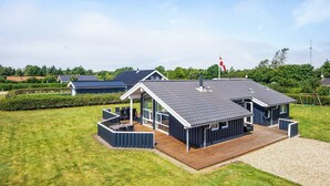Une maison moderne dotée d’une grande terrasse, d’un espace extérieur couvert et d’un drapeau sur le toit.