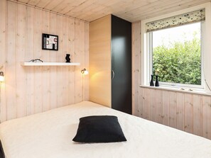 A bedroom with a bed, a black pillow, a white wall with a picture, a window with a view of greenery, and a wooden door. - 5 Star Holiday Home in Fjerritslev (Fjerritslev)
