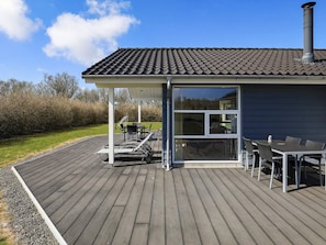 A covered outdoor deck with a dining table and chairs, a grill, and a large window.