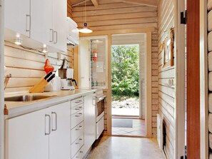 A kitchen with wooden walls, white cabinets, and a view of greenery outside.