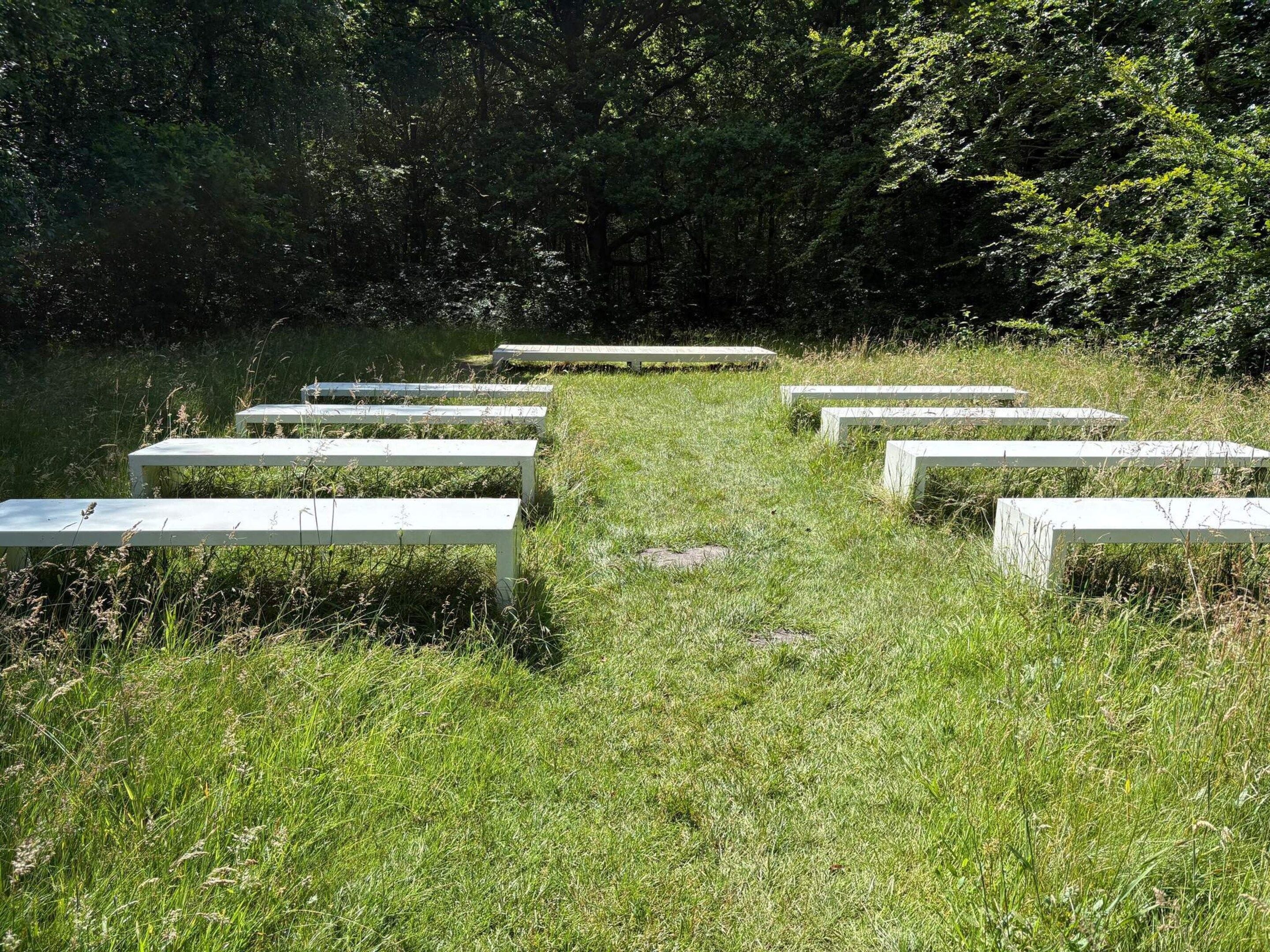 Ein grasbewachsener Bereich mit weißen Bänken, die halbkreisförmig angeordnet sind.